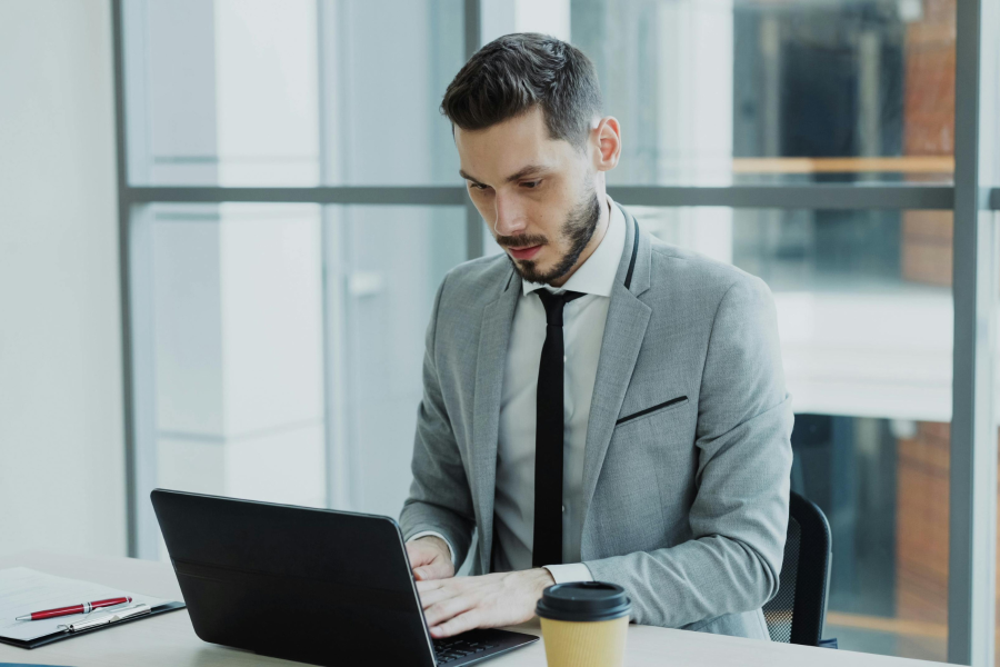 A professional wearing a grey blazer, sitting working on a laptop