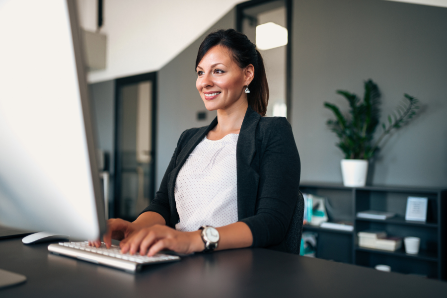 A professional wearing a black blazer, smiling at their computer screen