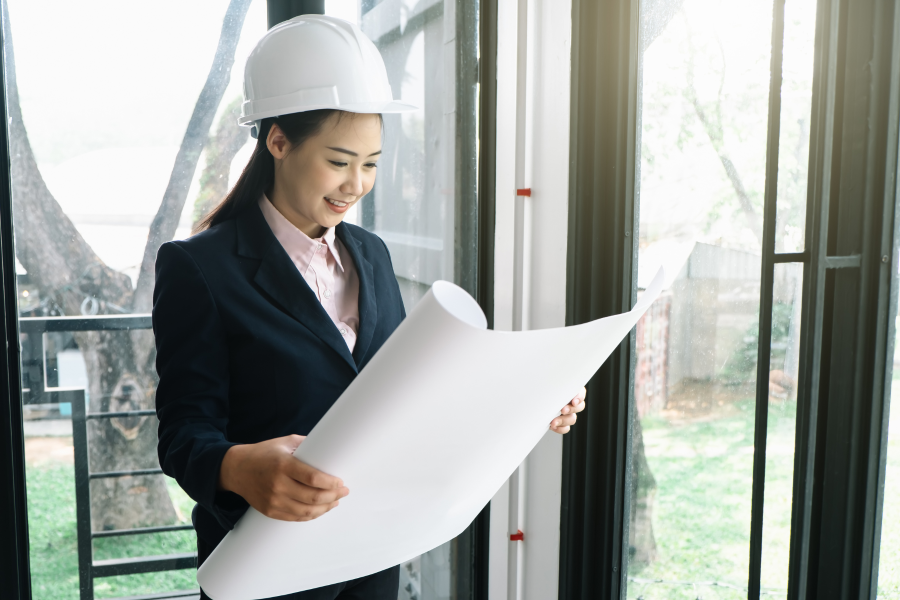 A professional wearing a suit and white hard hat, looking at a large piece of paper