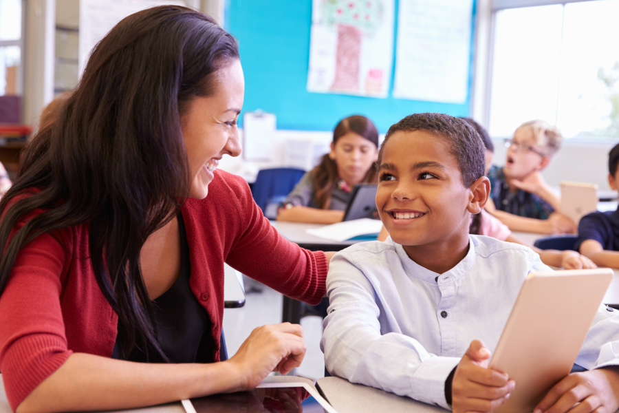 A professional in a red cardigan, smiling at a young student who holds a digital device