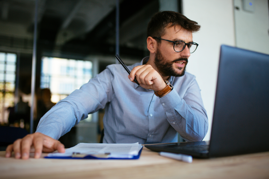 A professional wearing a blue shirt and glasses, looking at a laptop screen
