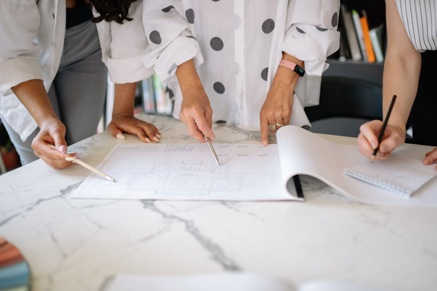 The hands of three professionals looking at paper and writing in a notebook