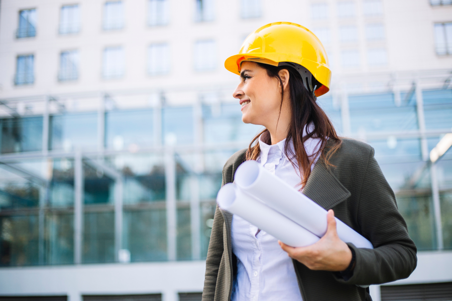 A professional wearing a yellow hard hat, holding two rolled up pieces of paper under their arm