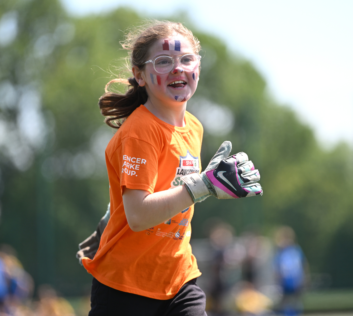 A child wearing glasses and an orange top, running outdoors