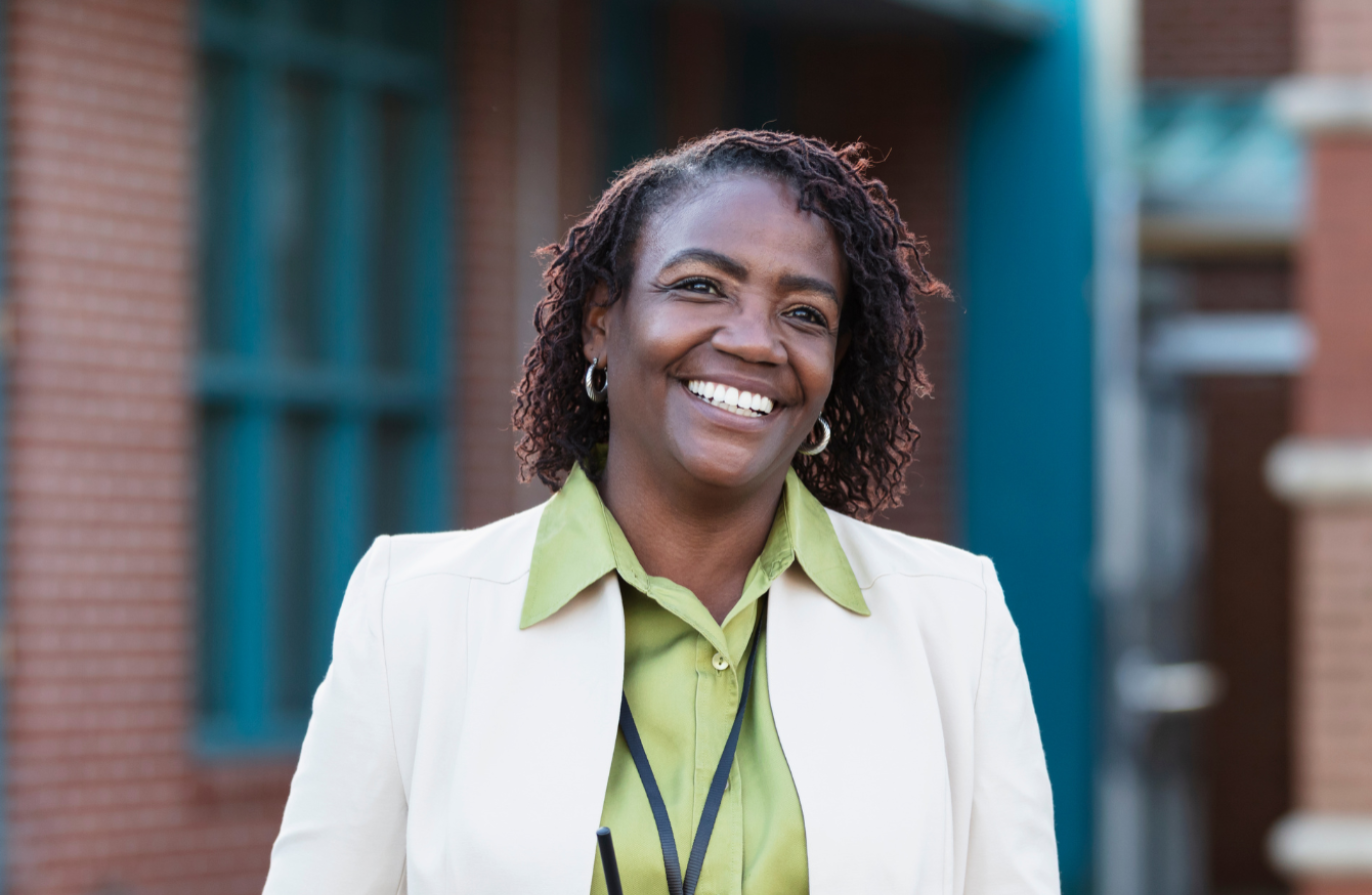 A professional wearing a green shirt and white blazer, smiling and holding a walkie talkie