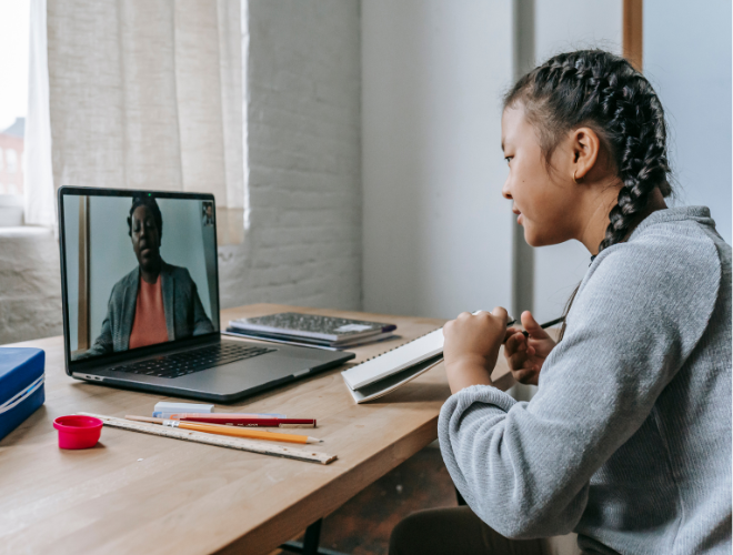 A young person sat at a desk using their laptop for an online meeting with another individual