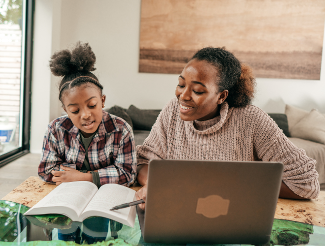An adult and child sat together by a laptop, reading a book