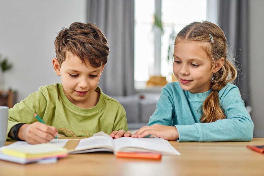 Two young children sitting and writing in a notebook together