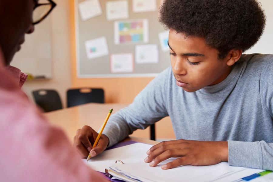 Tutor overlooking a student writing on a piece of paper