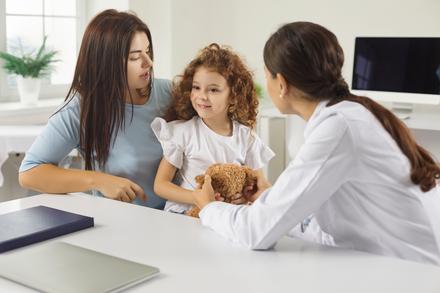 A child holding a teddy bear, sitting between two adults