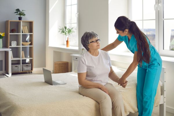 A female care assistant helping an elderly lady who is sat on a bed