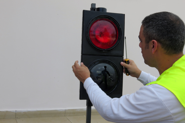 A male wearing a high vis jacket screwing on the front of a traffic light